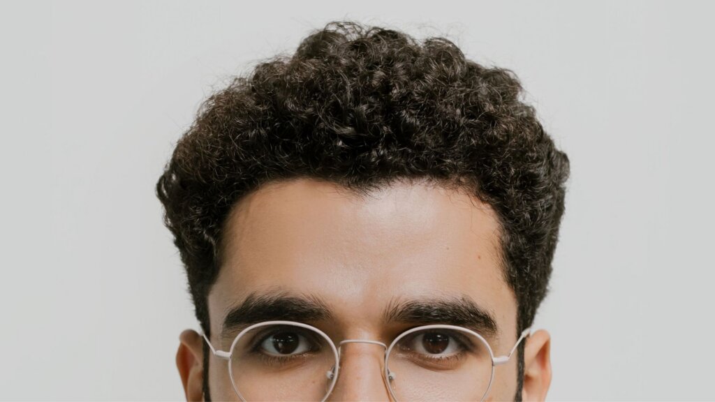 Detailed close-up portrait of a man with curly hair and eyeglasses.