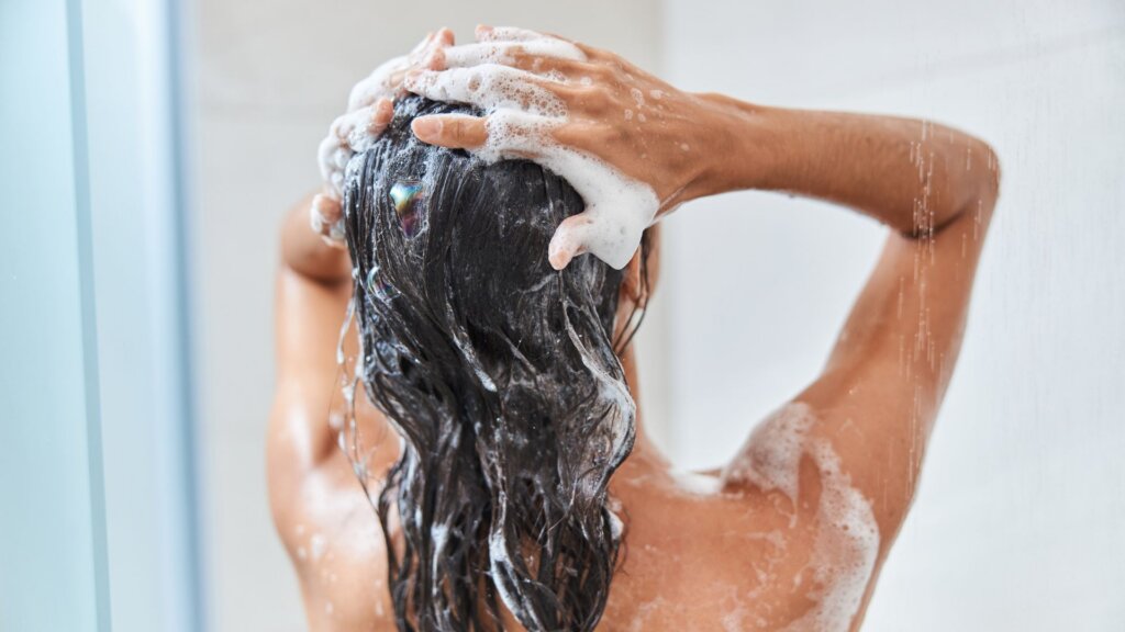 A woman shampooing wet hair under the shower.