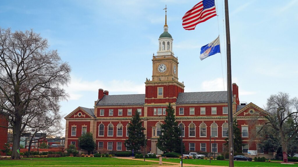 A red brick building with white columns and a domed tower on the Howard University campus, with a paved walkway and trees in the foreground.