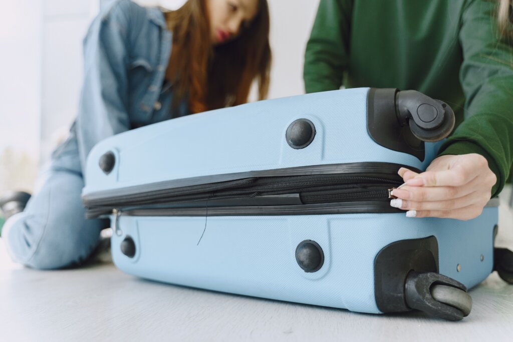 Travelers closing a suitcase while packing for an upcoming trip.