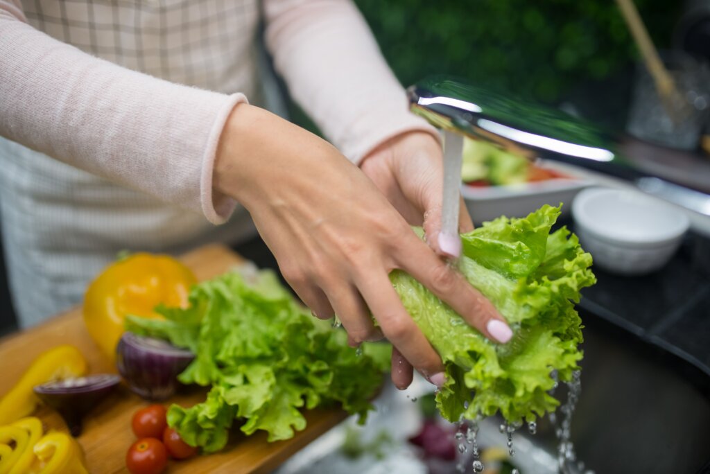Person washing fresh lettuce under running water.