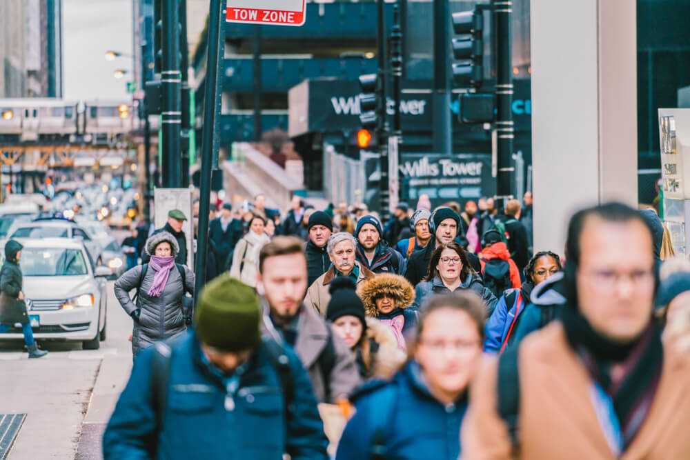 Pedestrians bundled in winter clothing walk along a busy downtown sidewalk during rush hour.