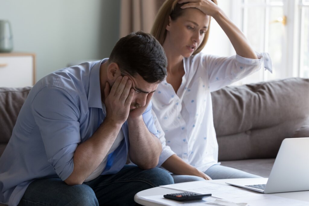 Couple reviewing financial documents and expenses on a laptop at home.