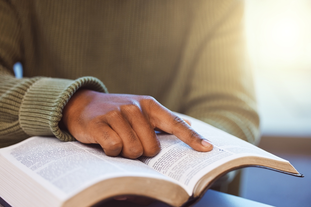 Close-up of a hand pointing to a passage while reading an open Bible.