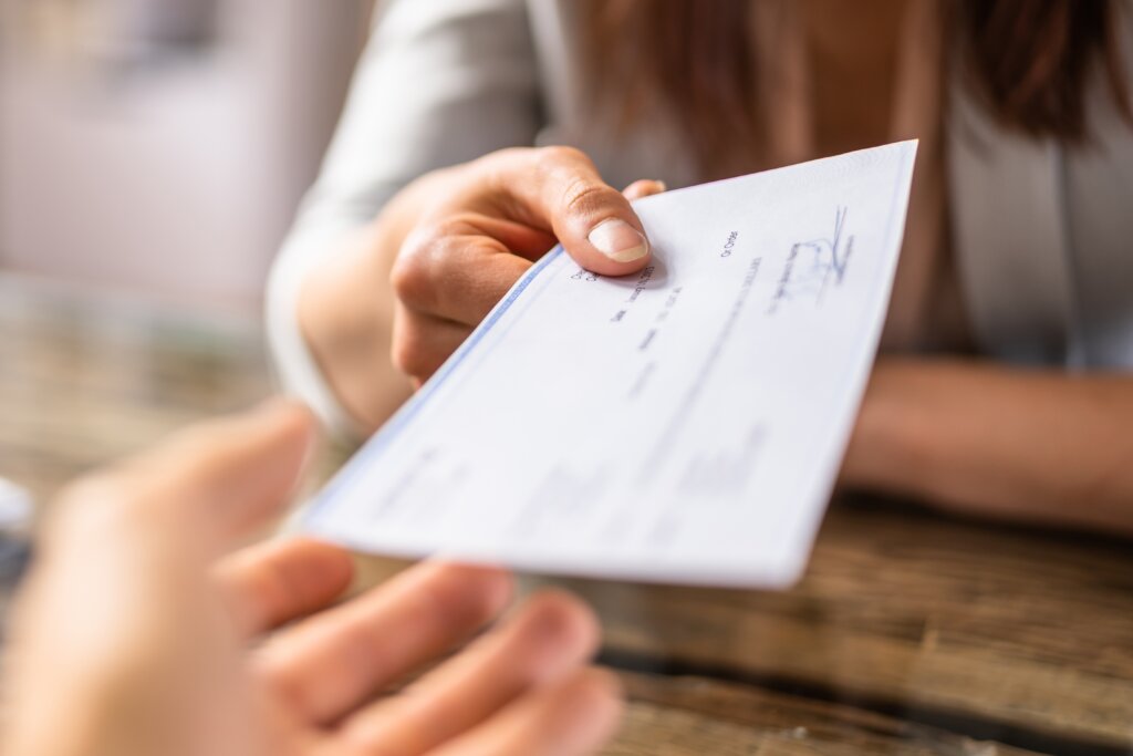 Close-up of a person handing a check to another person.