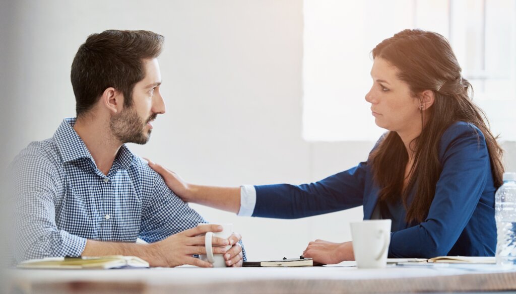 Coworkers having a serious conversation in an office, appearing concerned about a personal matter.