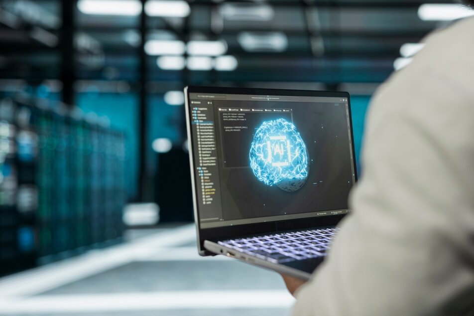 Person using a laptop displaying an artificial intelligence graphic in a data center.