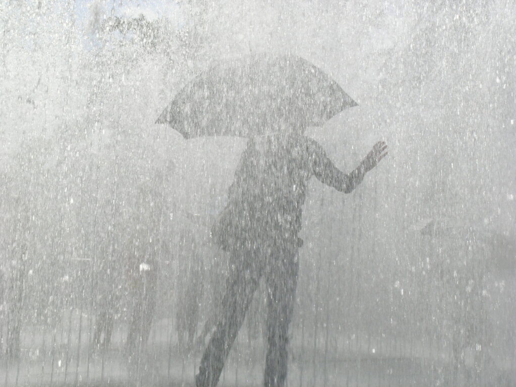 A person walks through heavy rain while holding an umbrella, illustrating intense rainfall and stormy weather.