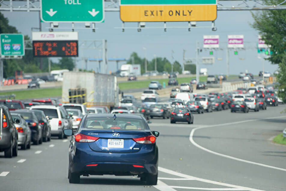 Traffic congestion approaching a highway exit with overhead toll and exit signs.