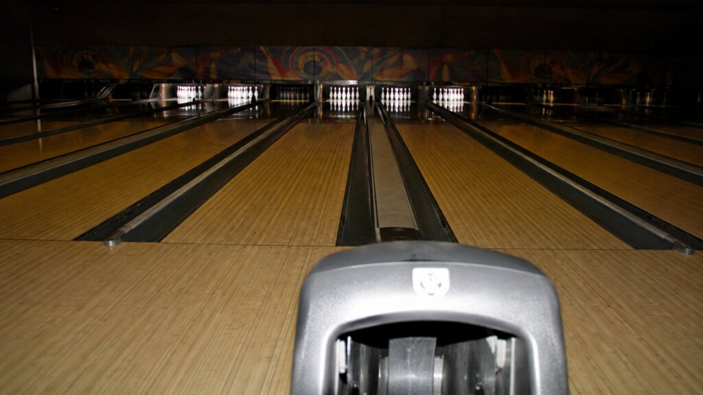 Several polished bowling lanes stretch toward illuminated white pins in a dark bowling alley.