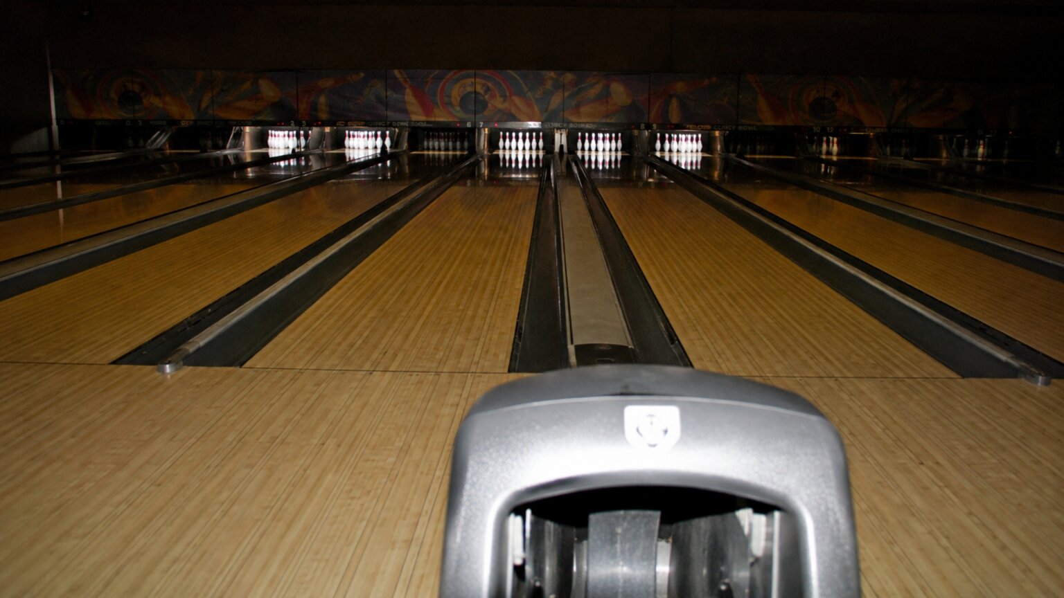 Several polished bowling lanes stretch toward illuminated white pins in a dark bowling alley.
