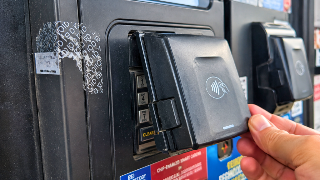 A person's hand checking a card skimmer overlay attached to a gas pump payment terminal.