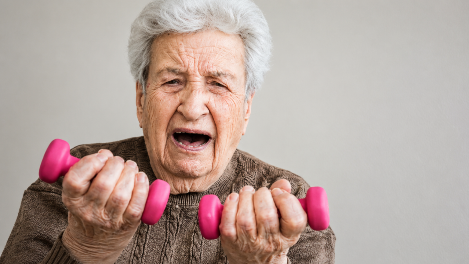 Image 1 Alt Text: An elderly woman holding small pink dumbbells and grimacing during a workout.