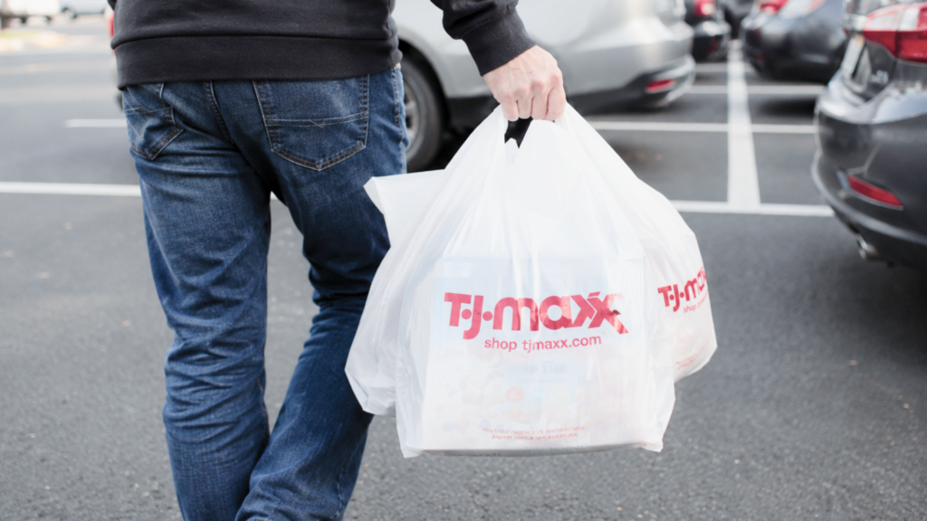 A shopper carrying white T.J. Maxx plastic shopping bags while walking through a parking lot.