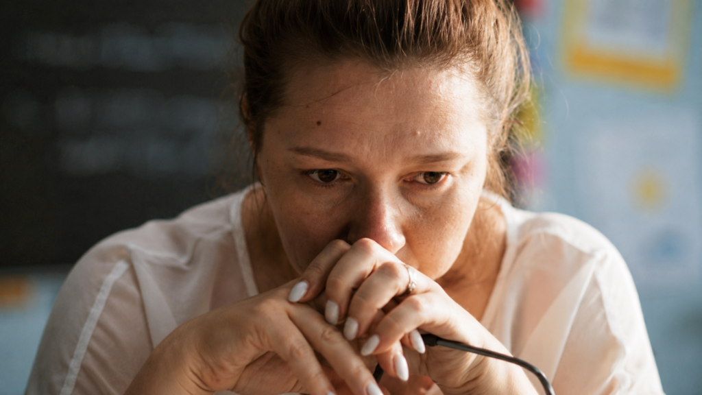A woman holding her face in her hands with a thoughtful expression while sitting at a desk.