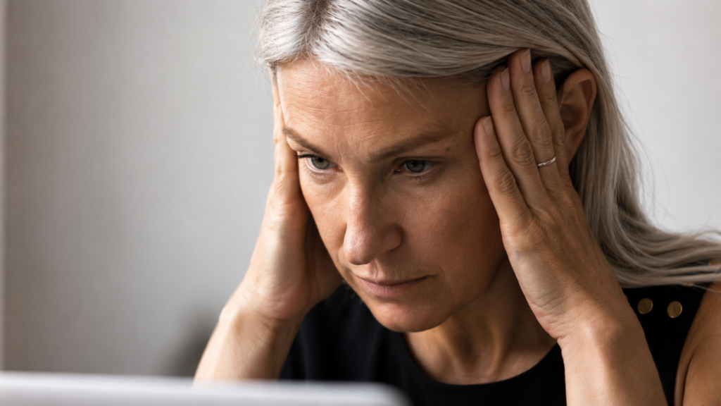 Stressed middle-aged woman holding her temples while looking at a computer screen.