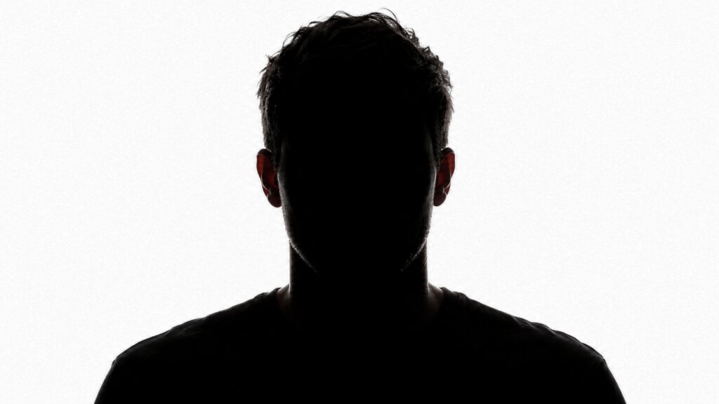 Dark silhouette of a person’s head and shoulders against a bright white background, leaving their facial features completely obscured.
