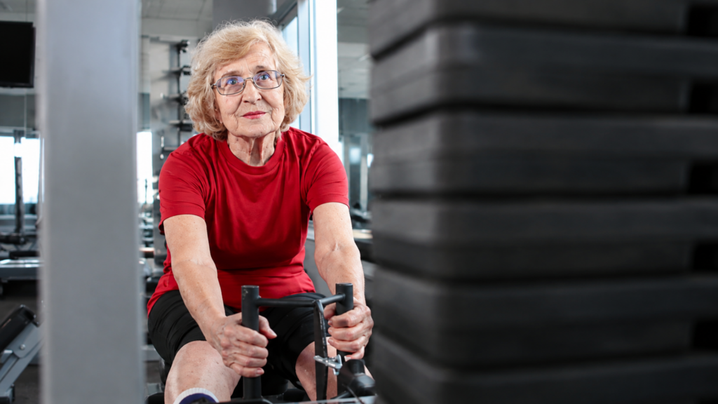 An elderly woman working out on a seated cable row machine in a gym.