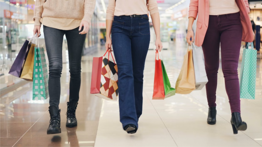 Three women carrying colorful shopping bags while walking through a shopping mall.