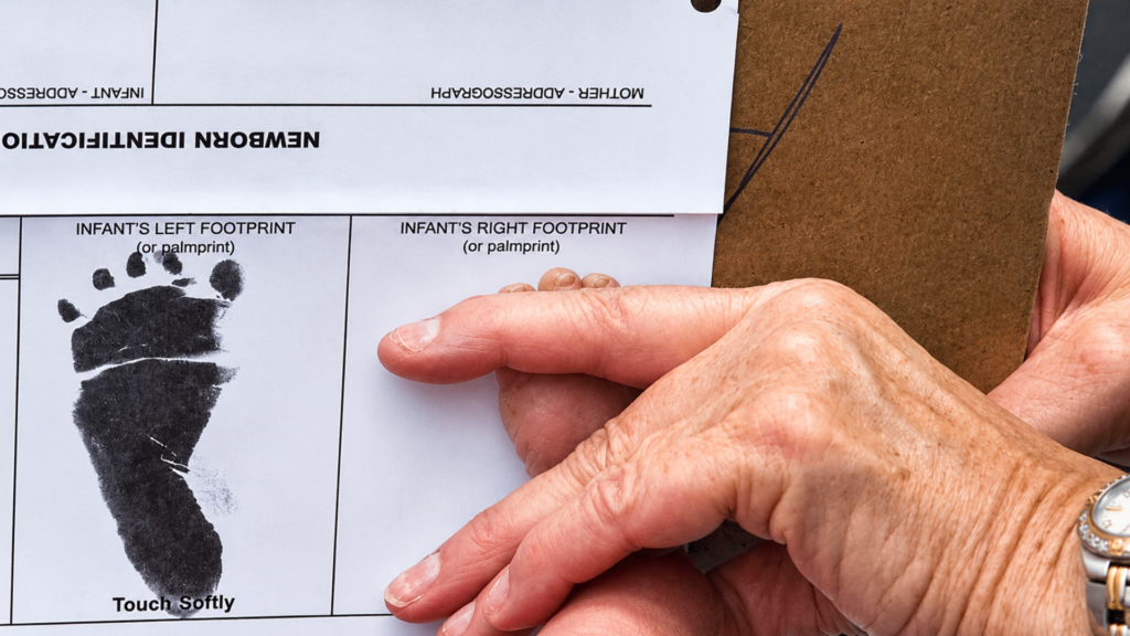 Close-up of a newborn identification form with a black ink footprint next to an infant's foot.