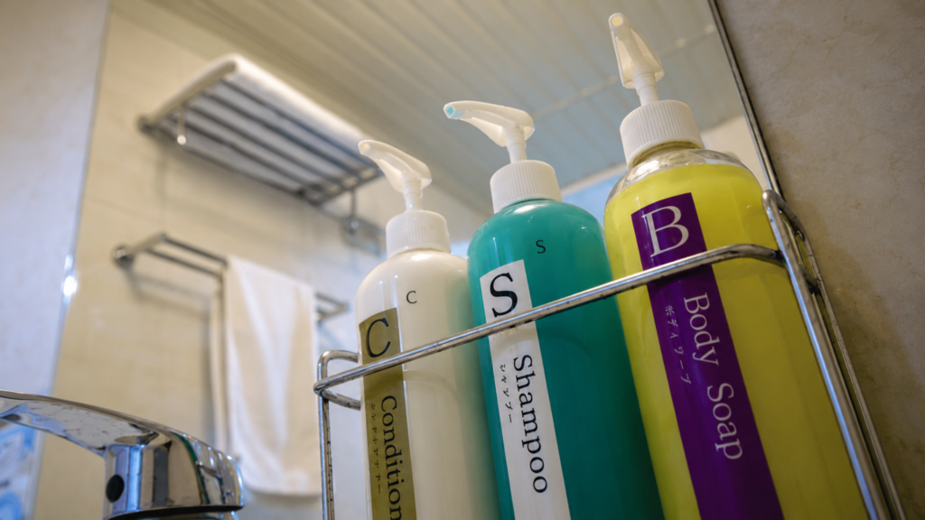 Three pump bottles labeled Conditioner, Shampoo, and Body Soap in a wire shower caddy.