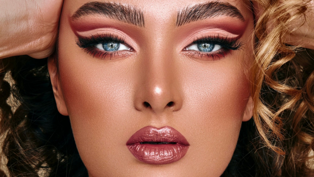 Close-up of a woman with striking makeup, blush swept high on the cheekbones for a lifted, sculpted look paired with soft, defined brows