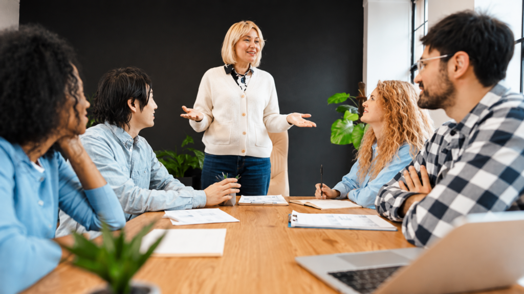 A woman leading a team discussion with colleagues around a conference table in an office meeting.