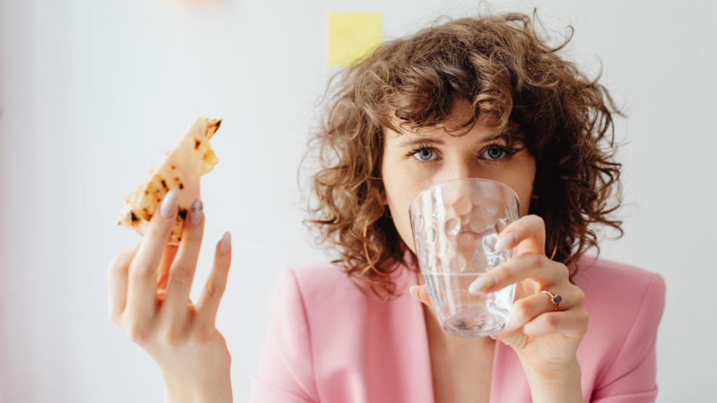Woman eating pizza and holding a glass of water.