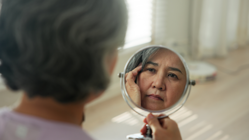 Woman inspecting her facial wrinkles in a small round mirror.