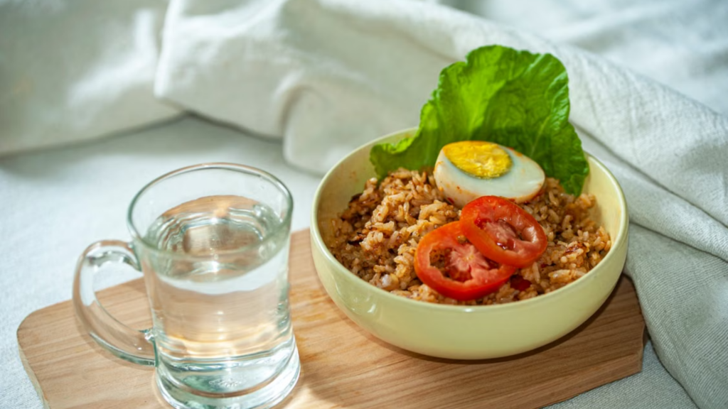 Bowl of fried rice topped with an egg and tomato slices next to a glass of water.