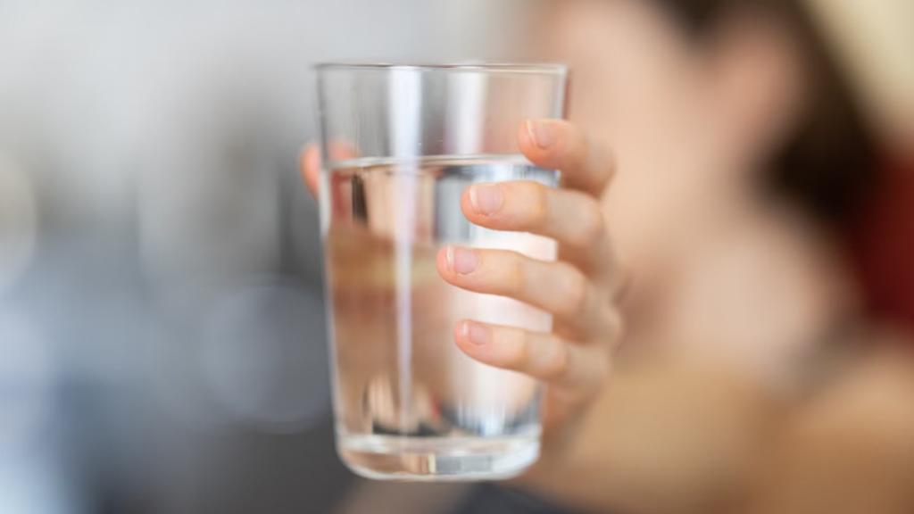 Close-up of a hand holding a clear glass of water.