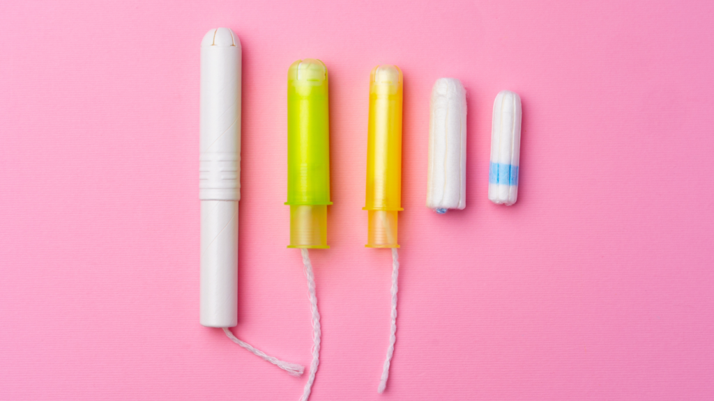 Five tampons of varying sizes, with plastic applicators and non-applicator options, arranged neatly against a bright pink background.