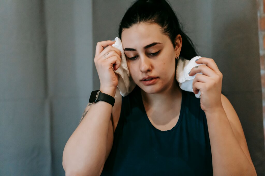 Woman wiping sweat from her face and neck with a towel indoors.