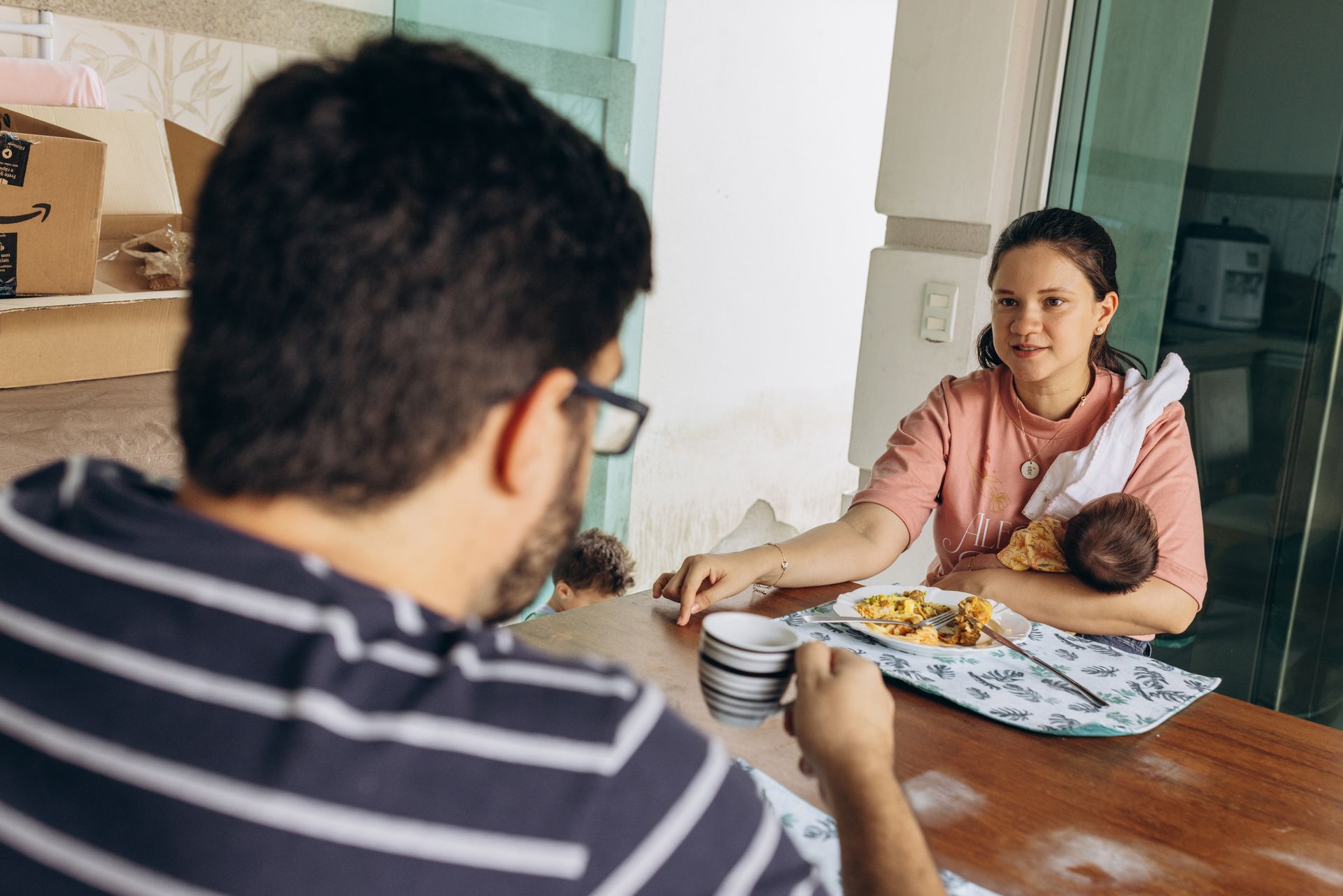 Woman holds a baby while talking with a man across a dining table.
