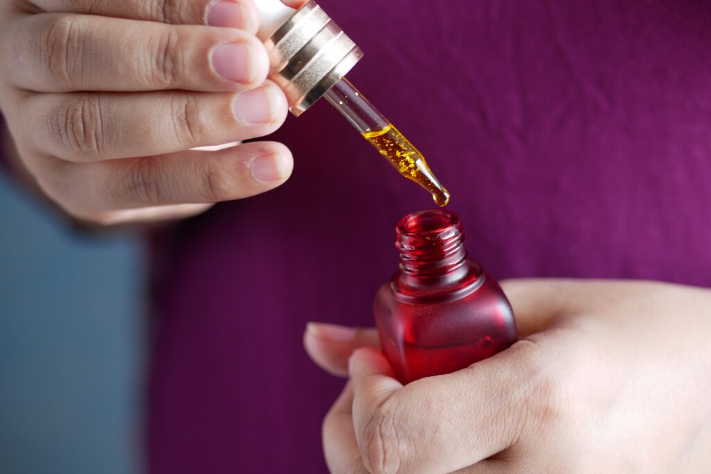 Hands dropping serum from a dropper into a red glass bottle; a generic representation, not an actual photo of Linlo Beauty product.