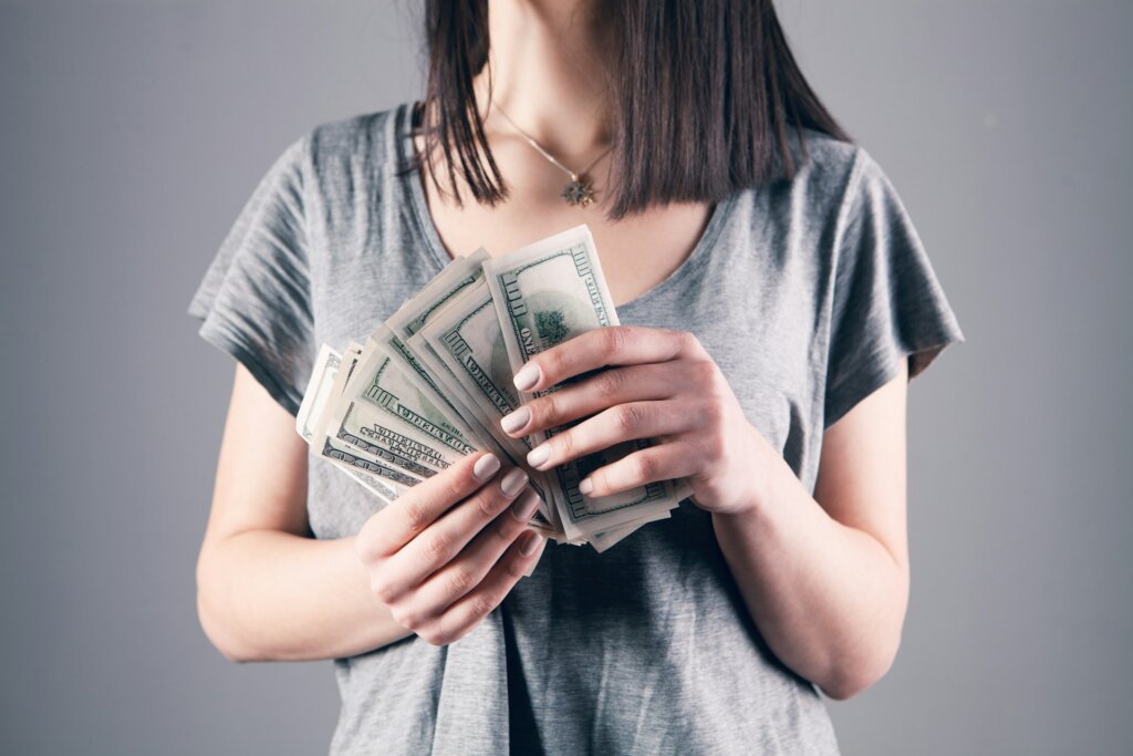 Woman holds a stack of U.S. $100 bills in both hands.