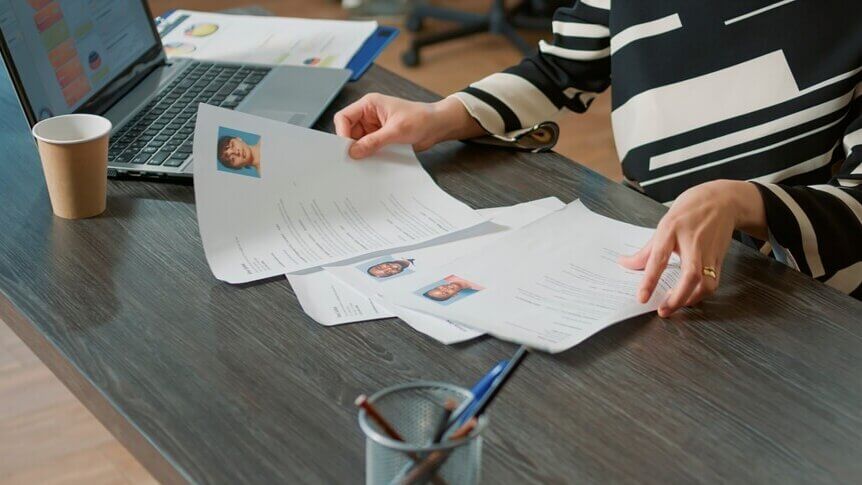 Hiring manager reviews printed résumés at a desk with a laptop during the hiring process.
