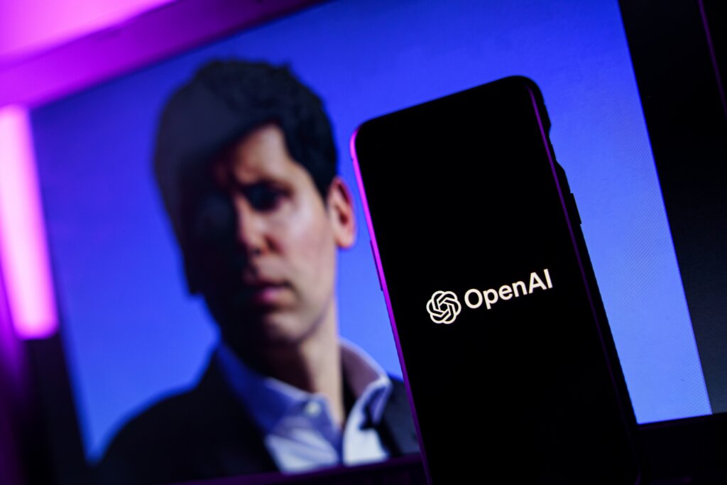 OpenAI logo displayed on a smartphone with Sam Altman in the background.