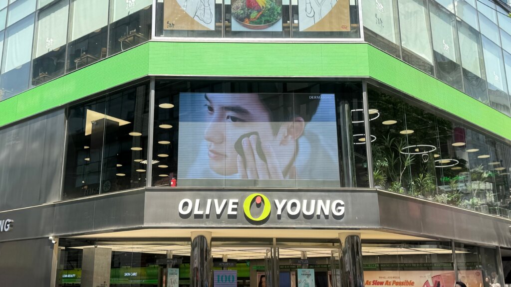 Exterior of an Olive Young beauty store with its green-and-black storefront sign and a large digital skincare advertisement above the entrance.