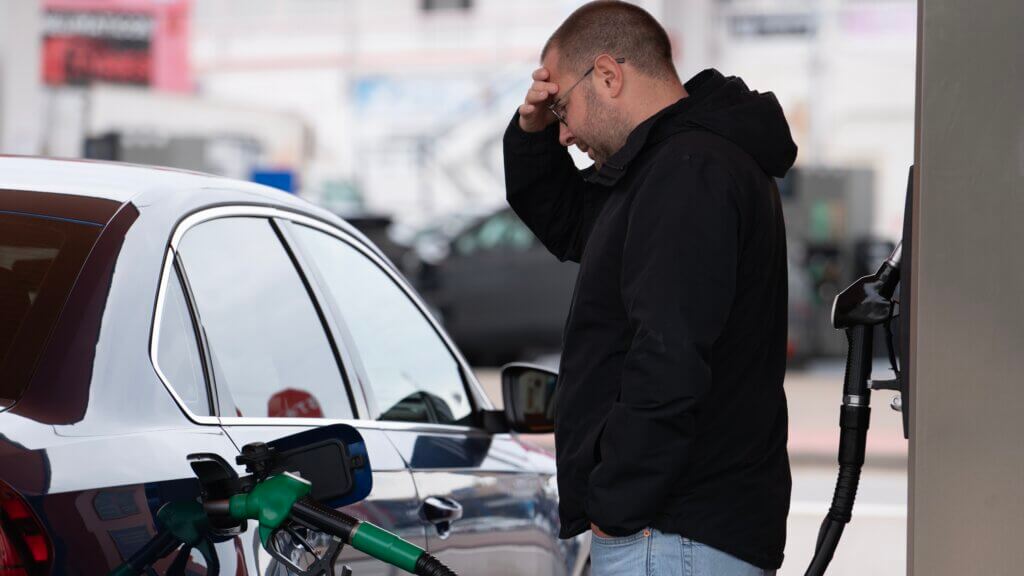 Concerned driver pauses while refueling a car at a gas station amid rising fuel costs.
