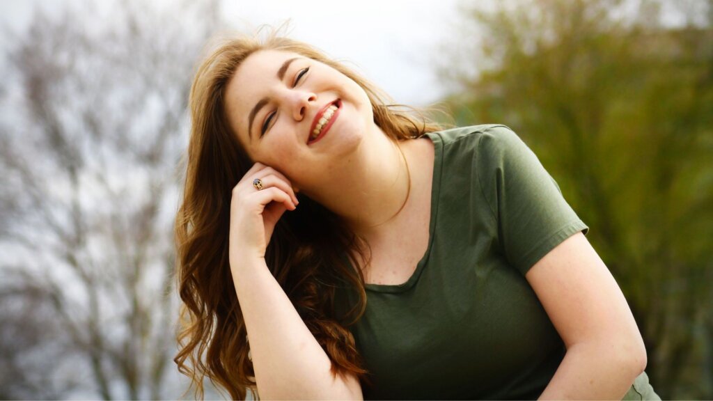 Woman with long brown hair smiling outdoors while wearing a green shirt.