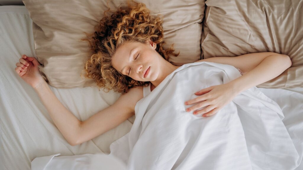 Woman sleeping on her back in bed under white sheets.