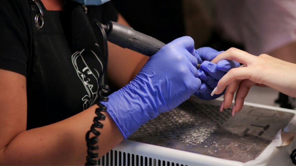Nail technician using an electric nail drill during a manicure.
