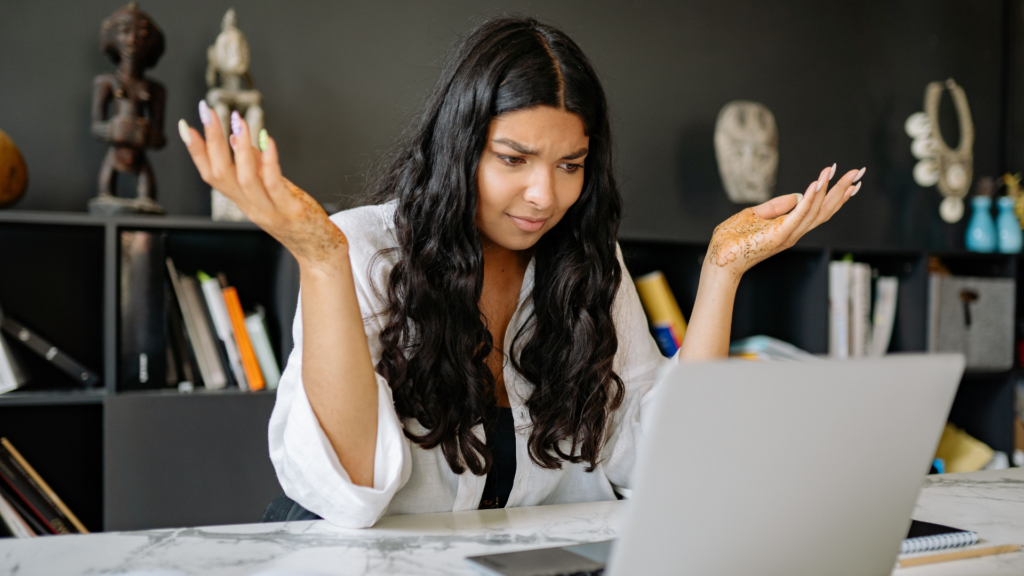 A woman at an office desk looks frustrated while working on her laptop. Modern office setting.