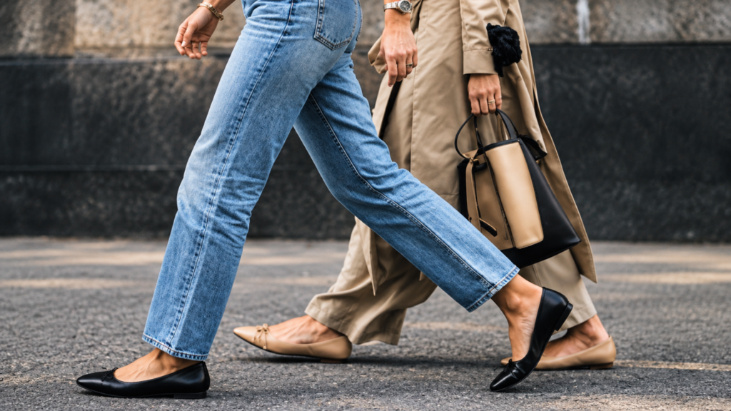 Low-angle shot of two people walking side-by-side in flat shoes, one wearing blue jeans and black ballet flats.