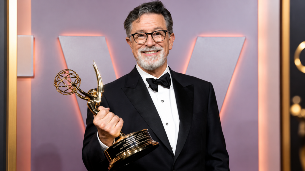 Stephen Colbert wearing a tuxedo and holding an Emmy Award trophy.