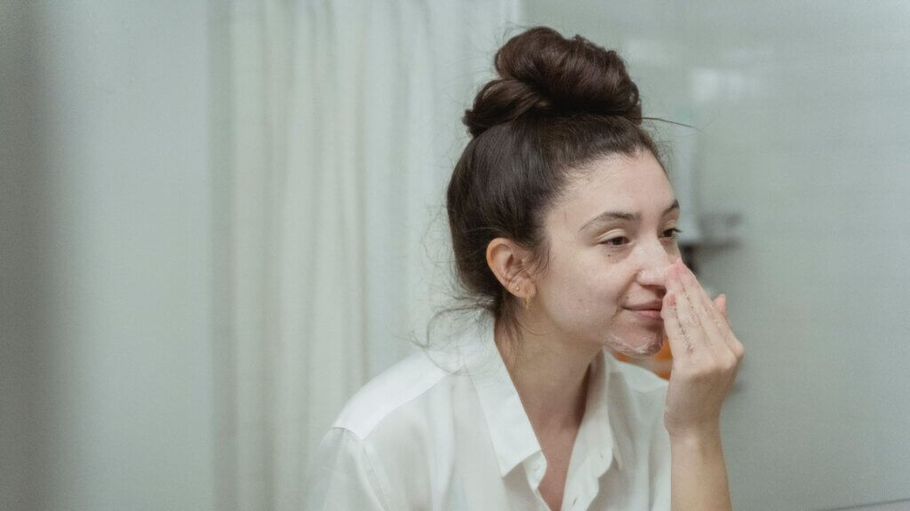 Woman applying a skincare product to her face in front of a mirror.
