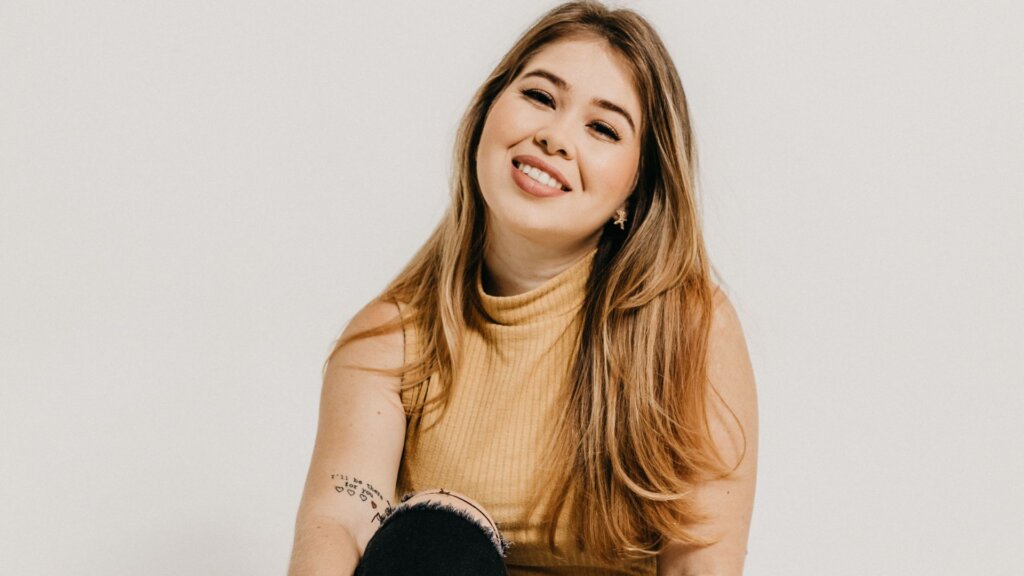 Woman with long highlighted hair smiling while seated against a white background.