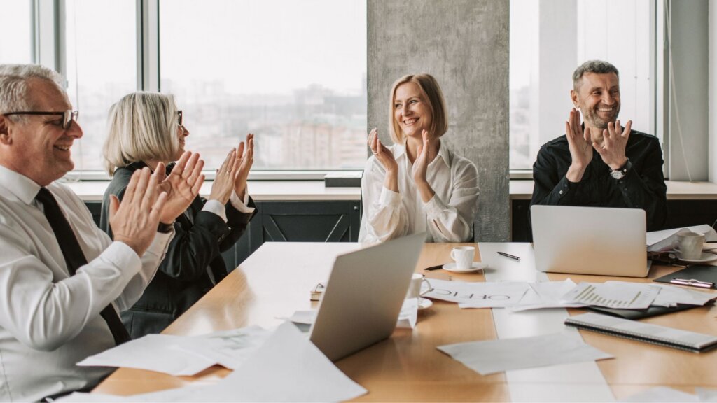 Business professionals applauding during a meeting around a conference table.