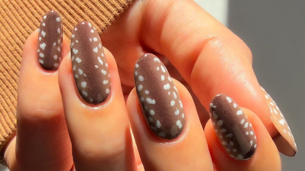 Long brown almond-shaped nails decorated with scattered white dots.
